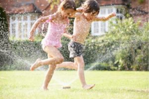 Two children playing in water on a lawn, showcasing summer fun—home services by The Meridian Company.