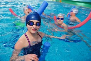 Children swimming in a pool with swim caps and goggles, enjoying home service tips from The Meridian Company.