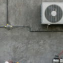 HVAC system installation with outdoor unit and connecting pipes against a concrete wall, relevant to heating services and energy efficiency tips.