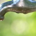 Close-up of an outdoor faucet with water dripping, highlighting plumbing fixtures for summer maintenance.