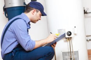 Plumber inspecting water heater and taking notes on maintenance checklist.