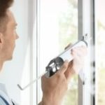 Man uses a caulking gun to seal a window during home improvement by The Meridian Company in Lansing, Michigan.