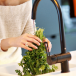 Person washing fresh parsley in a modern kitchen sink, highlighting cooking practices by The Meridian Company.