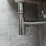 Pipe connection with chrome finish and water dripping, highlighting plumbing maintenance issues in Lansing's home services.
