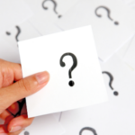 Hand holding a card with a question mark, surrounded by blurred cards, symbolizing HVAC and home improvement inquiries.