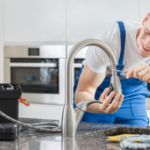 Plumber installing a metallic faucet in a modern kitchen, showcasing The Meridian Company's home improvement services.