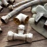 Plumbing tools and fittings on a wooden workbench, featuring metallic pipes, wrenches, and hoses from The Meridian Company.