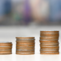 Stacks of metallic coins in varying heights against a blurred urban background, representing financial growth for homeowners.
