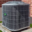 Air conditioning unit on concrete platform with metal grate, green light, against brick wall in Lansing, MI.