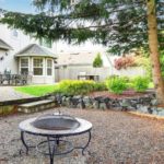 Fire pit surrounded by gravel, patio furniture, and a landscaped garden near a residential house from The Meridian Company.