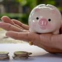 Hand holding a piggy bank with coins stacked, representing financial savings for HVAC maintenance in Lansing, MI.