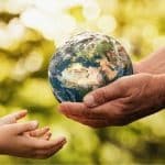 Child's hand reaching for an adult's hand holding a globe, symbolizing environmental responsibility and care for the Earth.