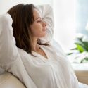 Woman relaxing at home with natural light, soft furnishings, and green plants.