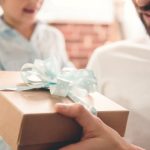 Two individuals exchanging a beautifully wrapped gift, highlighting connection and generosity amid a cozy setting.