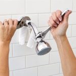 Hands holding a chrome showerhead during maintenance, part of The Meridian Company services in Lansing, MI.