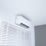 Sleek air conditioning unit mounted on a wall with window blinds, showcasing modern design for energy-efficient home comfort.