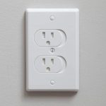 Electrical outlet in a light wall with a white cover plate and standard grounded two-slot design for home efficiency.