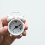 Hand holding a small white alarm clock with large numbers, representing The Meridian Company’s focus on home efficiency.