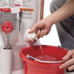 Person pouring water into a red bucket from a green dispenser, illustrating maintenance tasks by The Meridian Company.