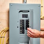 Electrical panel with circuit breakers and display, hand operating switch, and yellow wires for home safety maintenance.