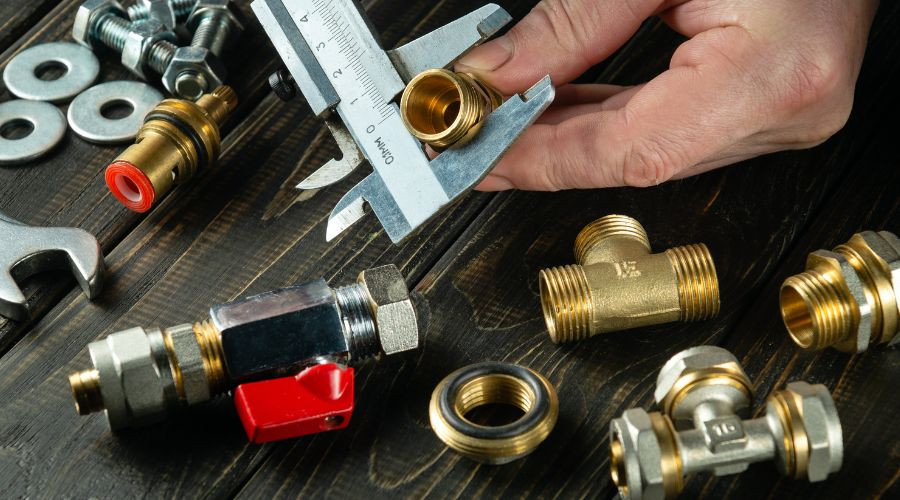 Hand holding a caliper with plumbing fittings, wrenches, and valves for home maintenance solutions by The Meridian Company.
