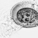 Drainage outlet with circular metal drain holes and flowing water, highlighting water dynamics—related to plumbing services.