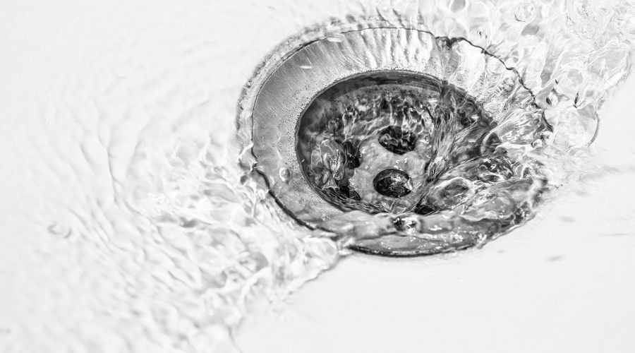 Metal drain with flowing water, showcasing plumbing solutions for home maintenance by The Meridian Company.