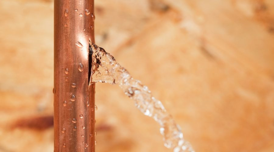 Copper pipe with a water leak, droplets forming on the surface, illustrating signs of plumbing issues related to water leaks and damage.